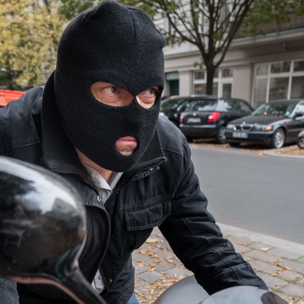 A person wearing a black knit balaclava that covers the head and neck, with only the eyes and mouth exposed.