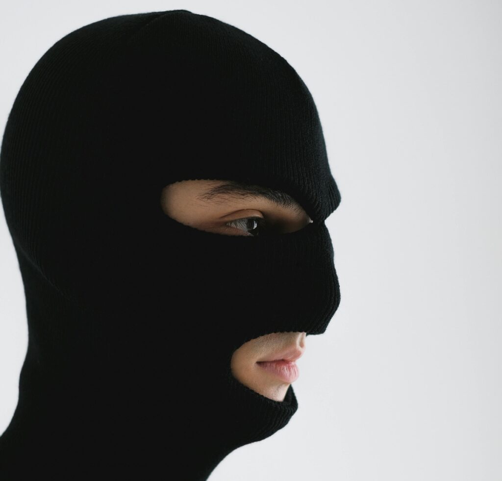 "Person wearing a black balaclava that covers the head and most of the face, with only the eyes and mouth revealed, against a light background."