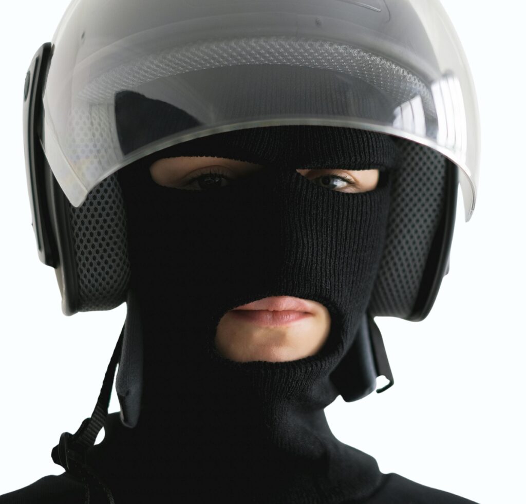 A person wearing a white motorcycle helmet with a black balaclava covering most of their face, leaving only the eyes and mouth visible.