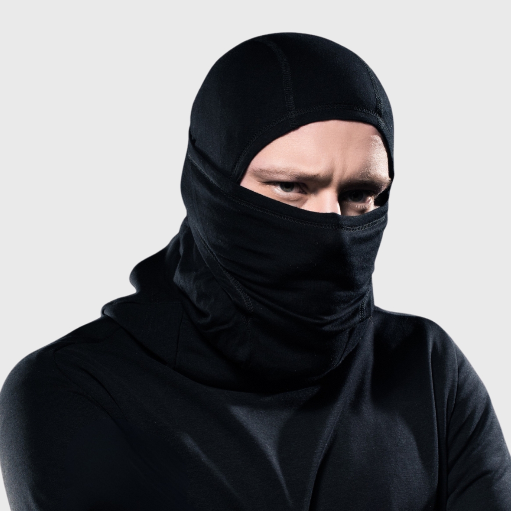 Person wearing a black balaclava-style neck gaiter covering most of the face except the eyes, with a black long-sleeve shirt on a light gray background.