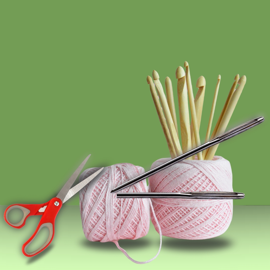A crocheting setup with two balls of pink yarn, several wooden knitting needles, a pair of red-handled scissors, and a metal knitting needle lying across the yarns, all against a green background.