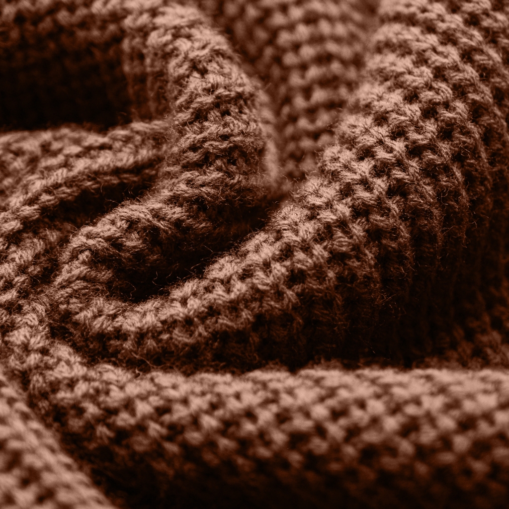 A close-up of soft, chunky knit fabric in a warm brown color, showcasing thick, textured stitches and folds that convey coziness and warmth.