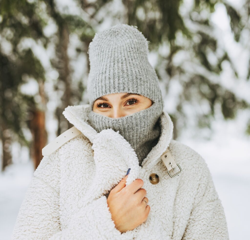 A person dressed warmly in a light gray knit balaclava, beanie, and fluffy white coat, with only their eyes visible.