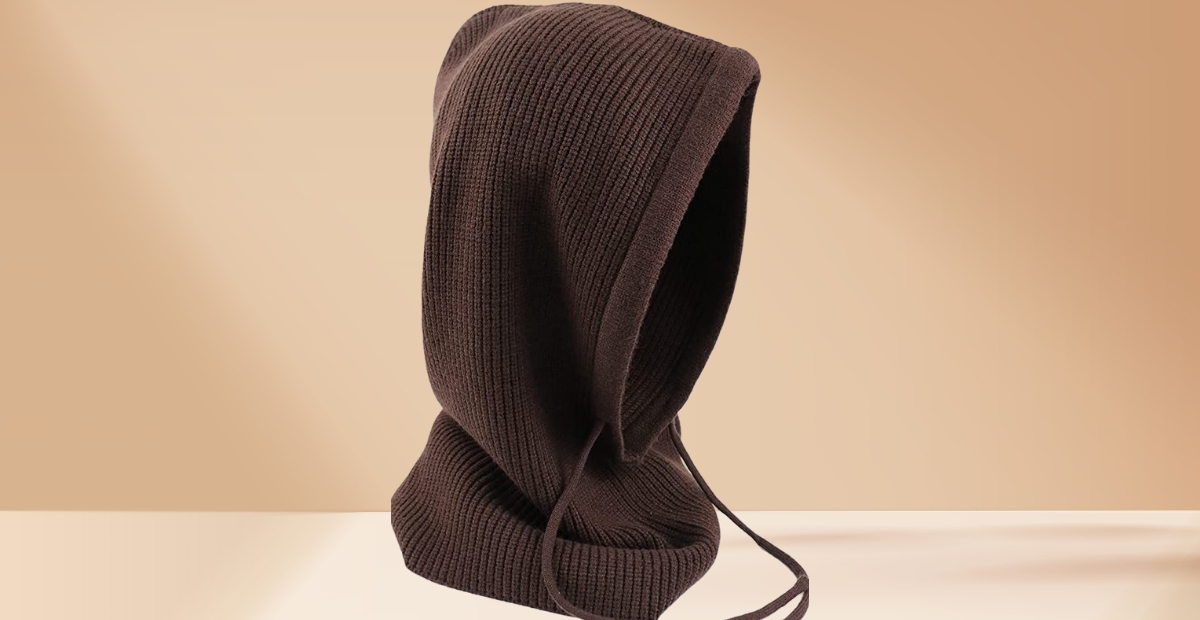 A dark brown knit balaclava with a hood and long drawstrings sits against a neutral beige background.