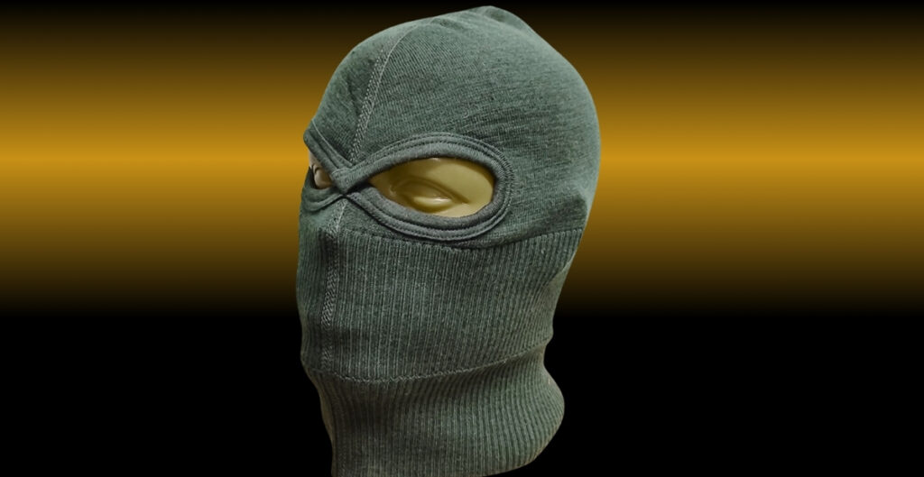 Green balaclava/ ski mask on a mannequin head, with a single eye opening visible, black-to-gold gradient background