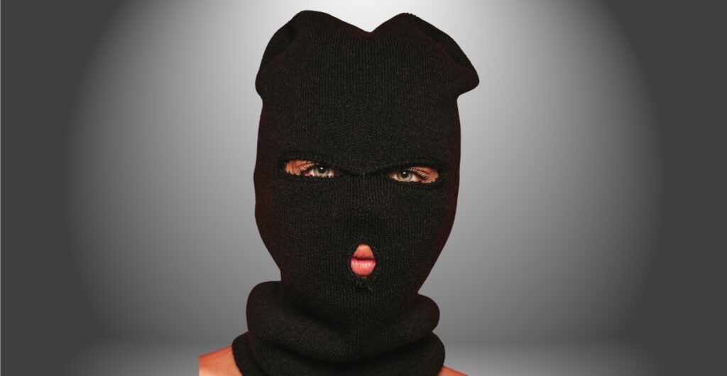 A person wearing a black ski mask that covers most of their face, with only the eyes and mouth visible.