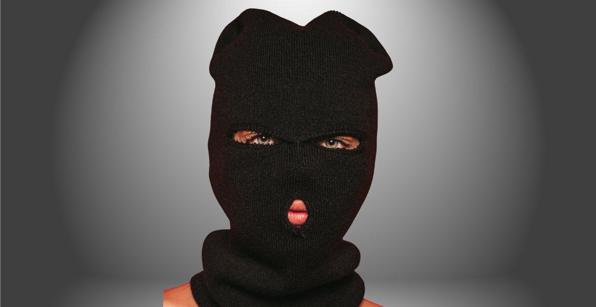 A person wearing a black ski mask that covers most of their face, with only the eyes and mouth visible.