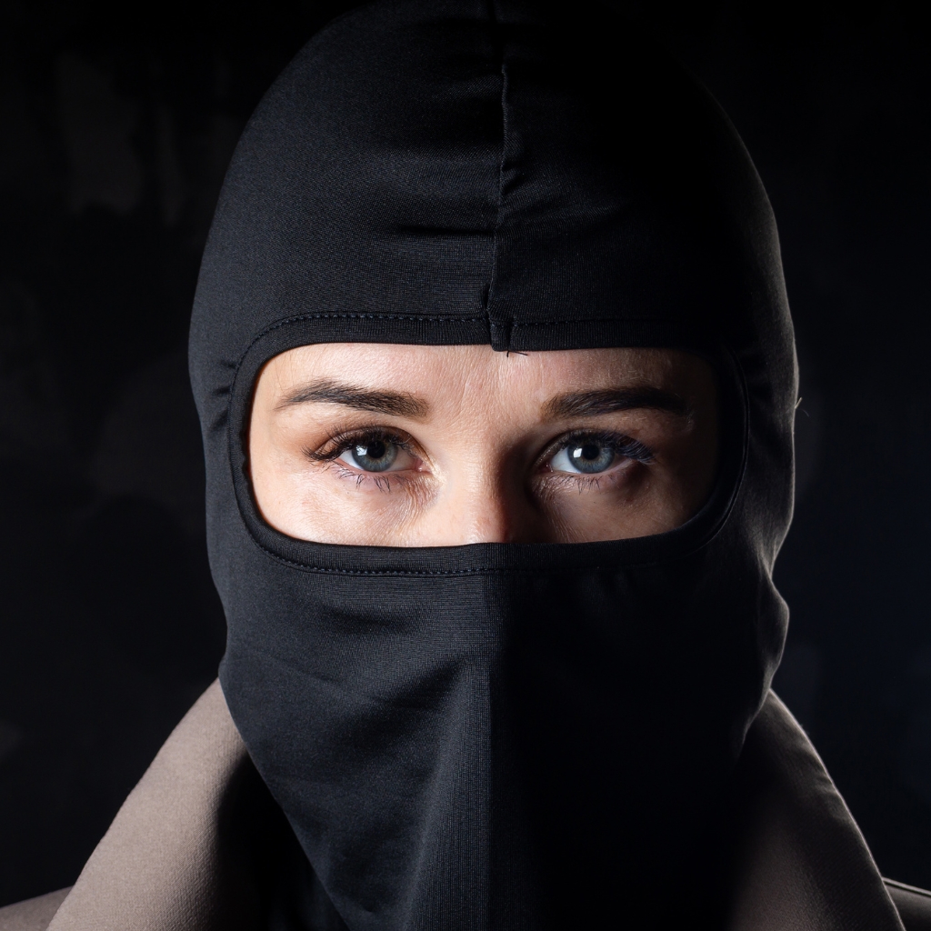 A person wearing a black balaclava that covers most of their face, leaving only the eyes visible.
