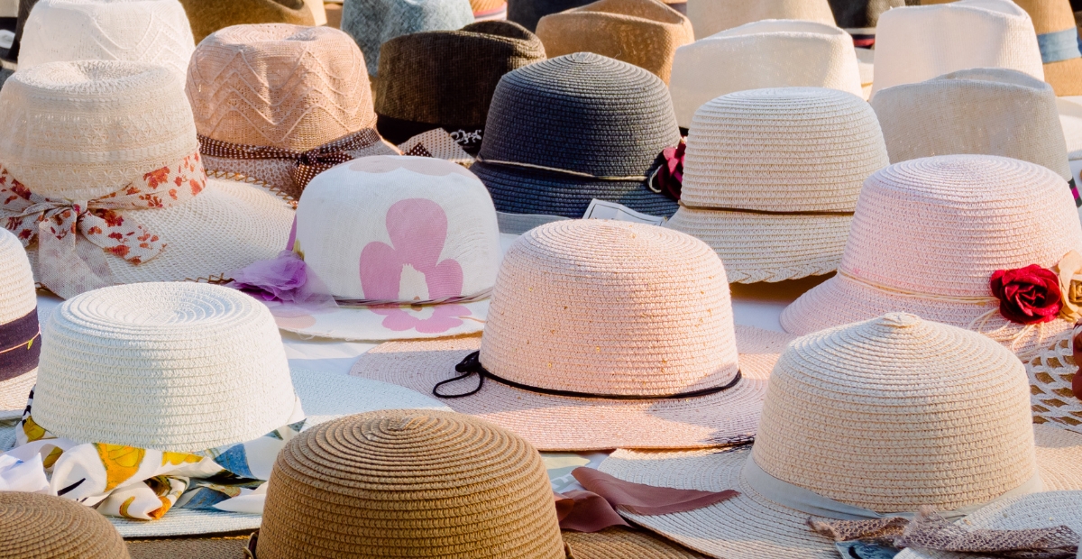 Una densa disposición de sombreros de paja de ala ancha en varios colores y estilos, algunos con cintas, lazos o adornos florales, muy juntos entre sí.