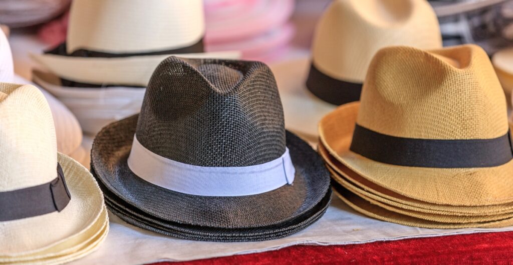 Eine Ausstellung von Trilby-Hüten in verschiedenen Farben (beige, schwarz und strohfarben), die auf einem Tisch angeordnet sind.