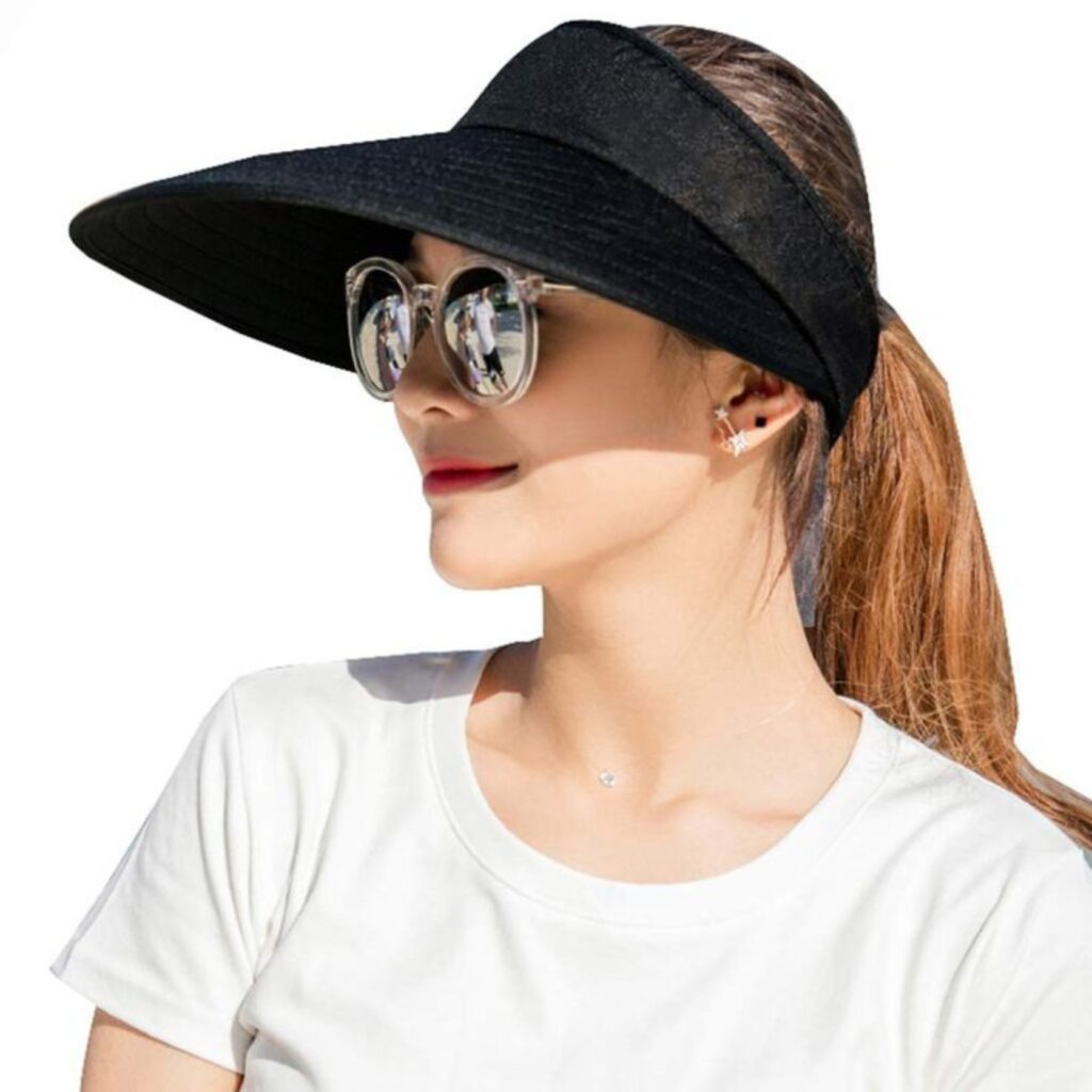 Femme portant un chapeau noir à large bord, des lunettes de soleil réfléchissantes oversize, un t-shirt blanc et une queue de cheval.