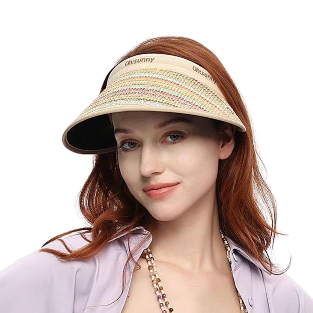 A woman with red hair wearing a beige woven visor hat. The hat has a wide curved brim and a decorative band with pastel colors, and the brand name “oh-sunny” on the front. She is smiling softly and wearing a light purple shirt.