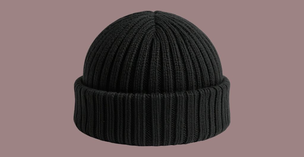 Black rib-knit beanie with a wide folded cuff, displayed against a muted mauve background