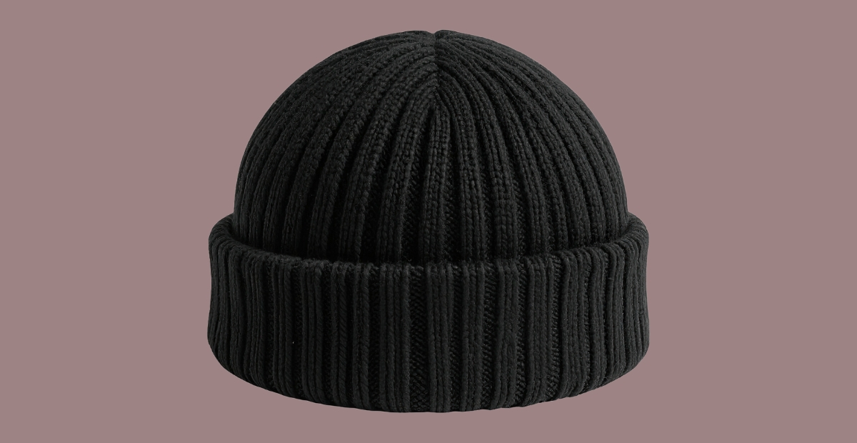 Black rib-knit beanie with a wide folded cuff, displayed against a muted mauve background