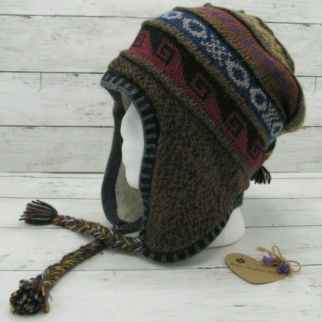 Gorro de invierno de punto con orejeras y borlas trenzadas, expuesto en una cabeza de maniquí blanca. El gorro presenta motivos marrones, grises, rojos y azules, con una borla multicolor a cada lado.