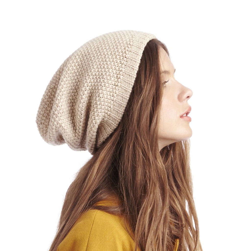 Una mujer joven con un gorro holgado de punto grueso de color beige, vista de perfil hacia la derecha.
