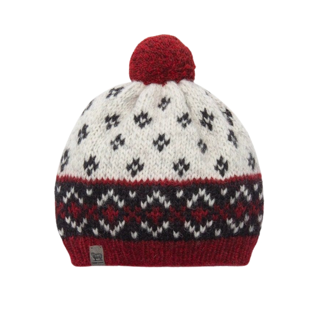 A knit beanie in white with navy diamond patterns and a red pom-pom on top, featuring a red ribbed band at the bottom.