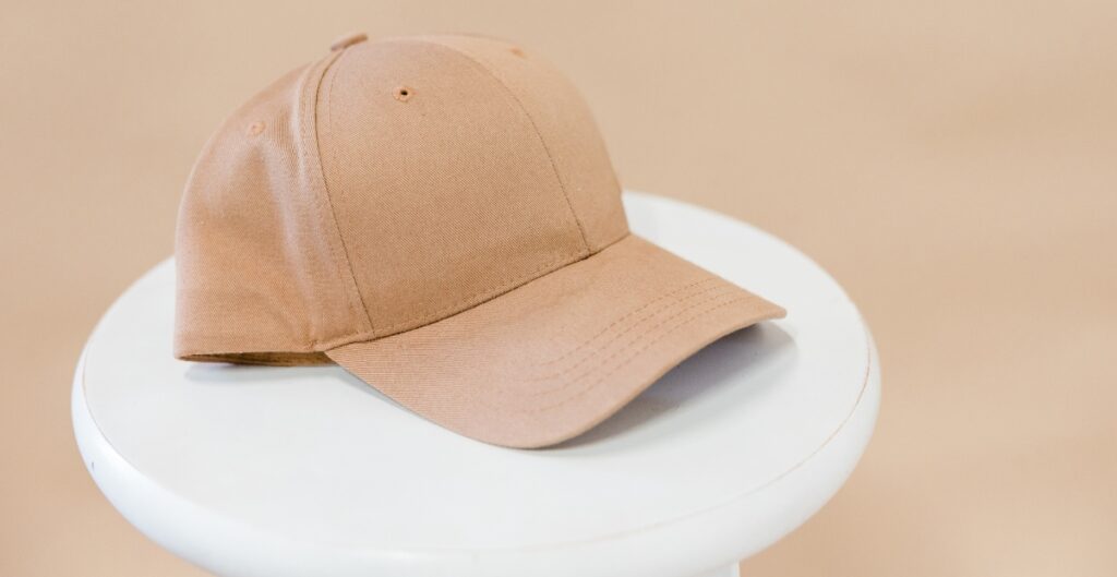 A light brown/beige six panel cap resting on a white, round pedestal.