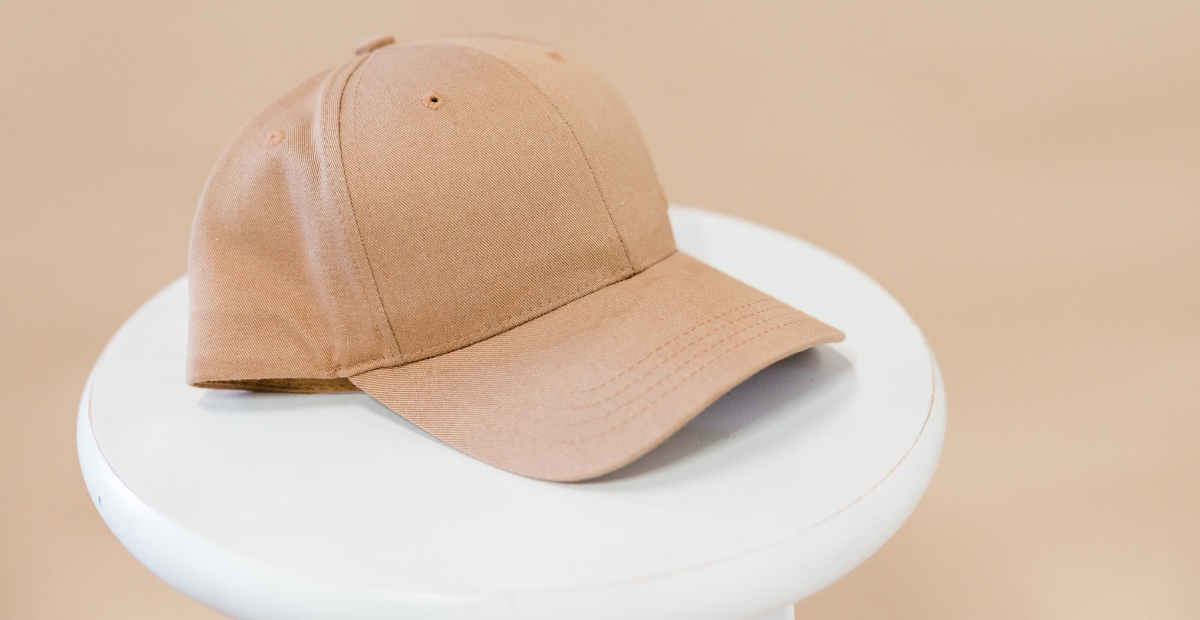 A light brown/beige six panel cap resting on a white, round pedestal.