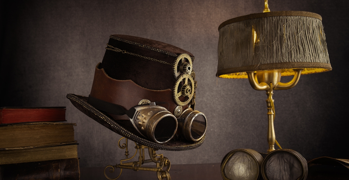 A vintage steampunk hat with brass gears and goggles sits on a decorative stand beside a brass and glass lamp. A stack of old books rests in the background, and a pair of round goggles lies nearby.