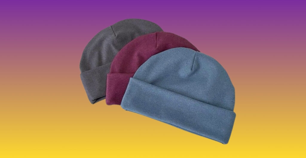 Three knit thermal beanies in gray, burgundy, and blue layered together against a gradient background.