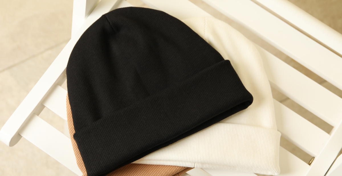 Una pila de gorros de cachemira suave en negro, crema y marrón claro, cuidadosamente doblados sobre una silla de madera blanca.