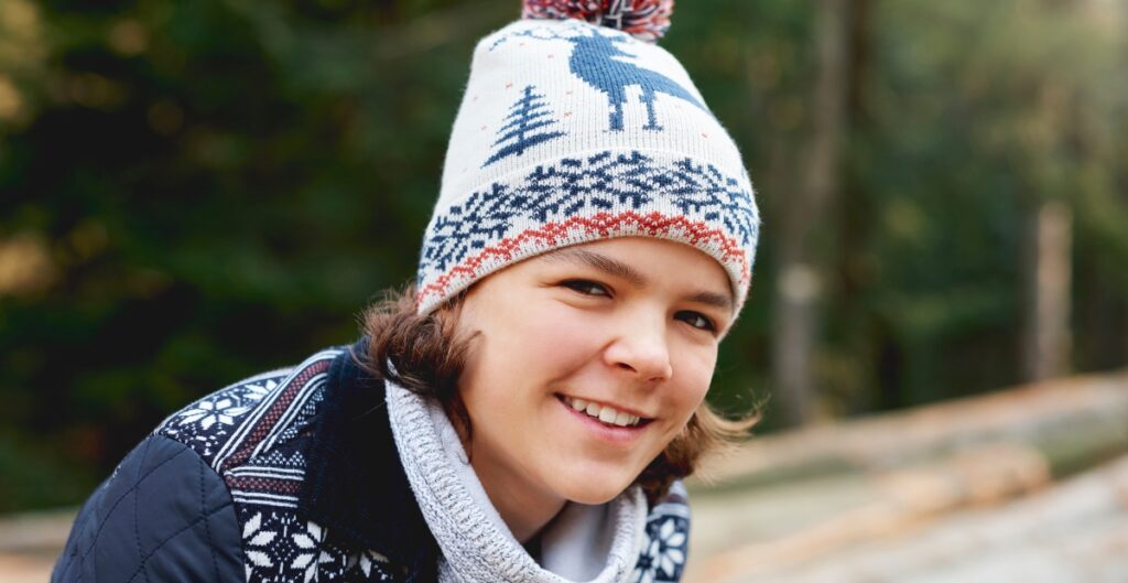 Smiling child wearing a white Fair Isle knit beanie with blue and red patterns.