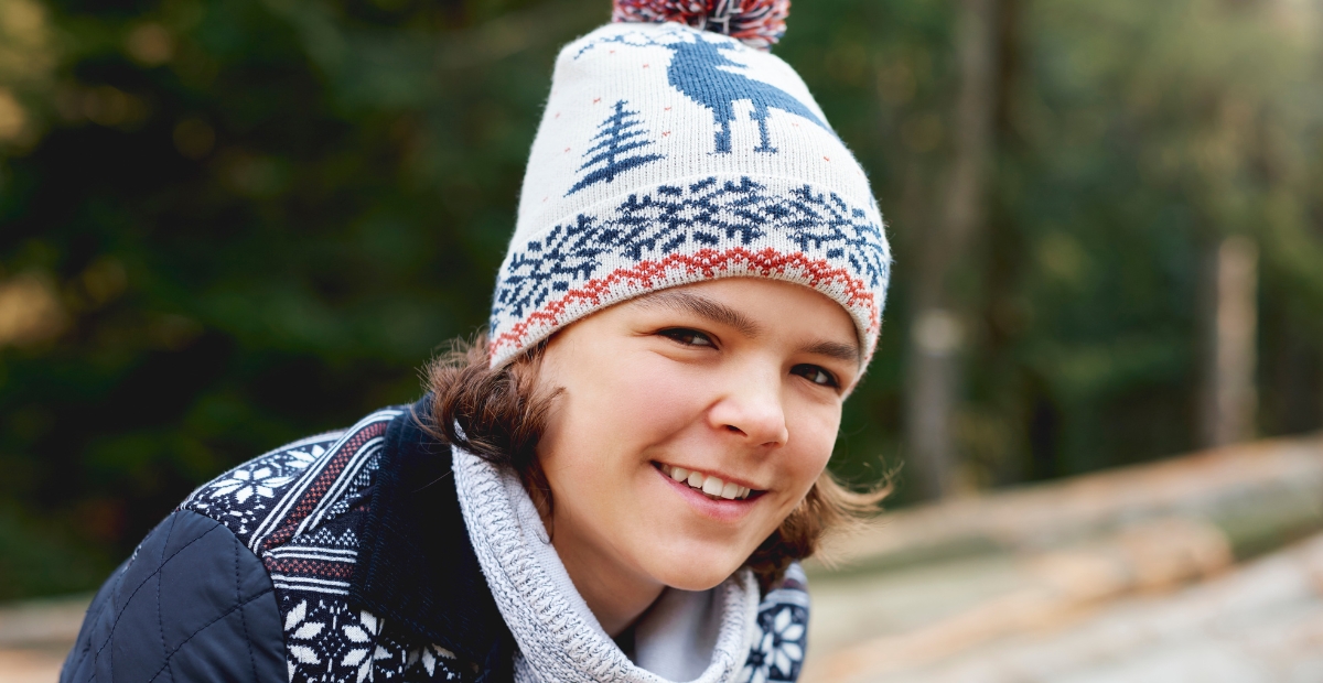 Smiling child wearing a white Fair Isle knit beanie with blue and red patterns.