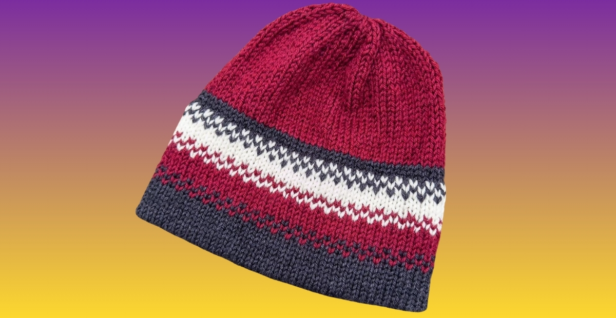 A knit beanie hat with red, white, and navy blue stripes on a gradient purple-to-yellow background.