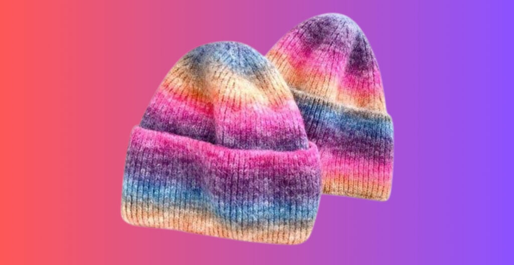 Two knit beanies with an ombre rainbow gradient from pink to purple against a pink-to-purple gradient background