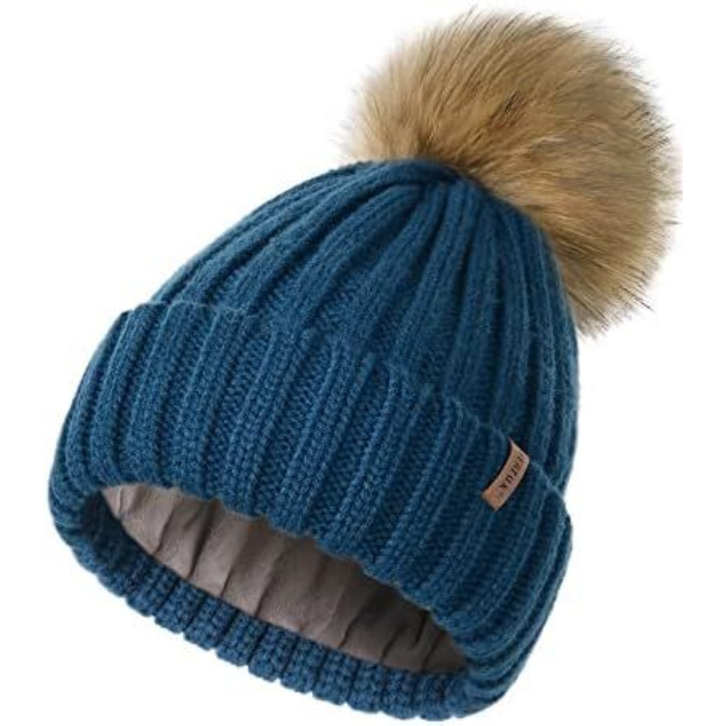A blue knit beanie with a large fluffy pom-pom on top and a soft, light-brown faux fur pom at the crown.