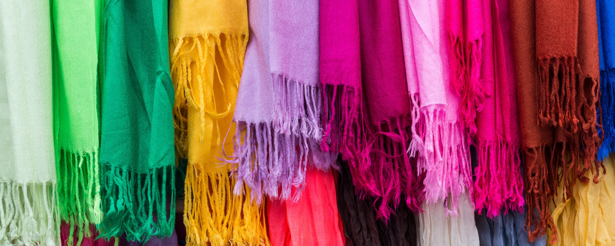 Rows of fringed scarves in bright green, yellow, pink, purple and red