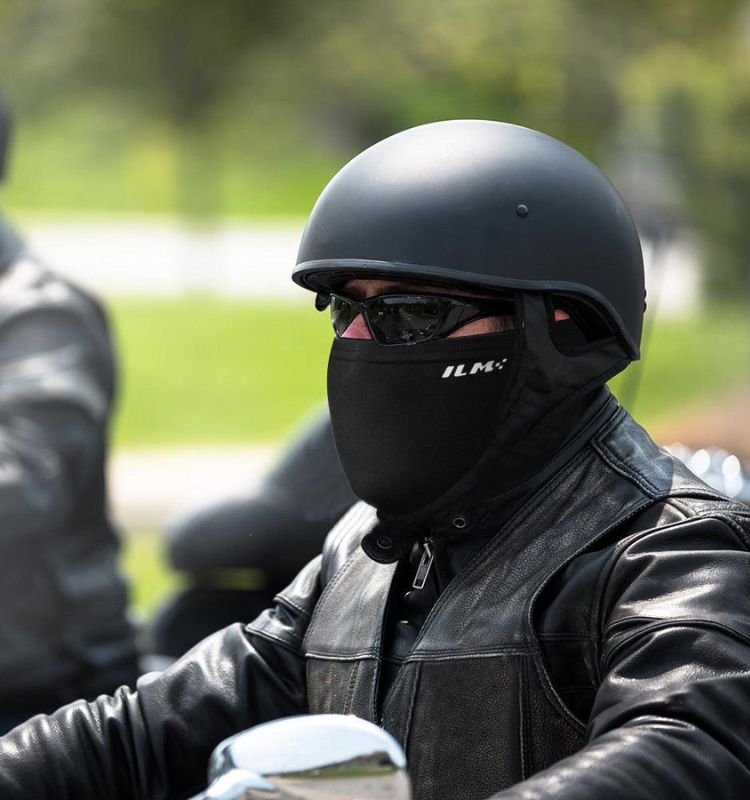 Man wearing a black bike ski mask and helmet while riding a motorcycle in cold weather.