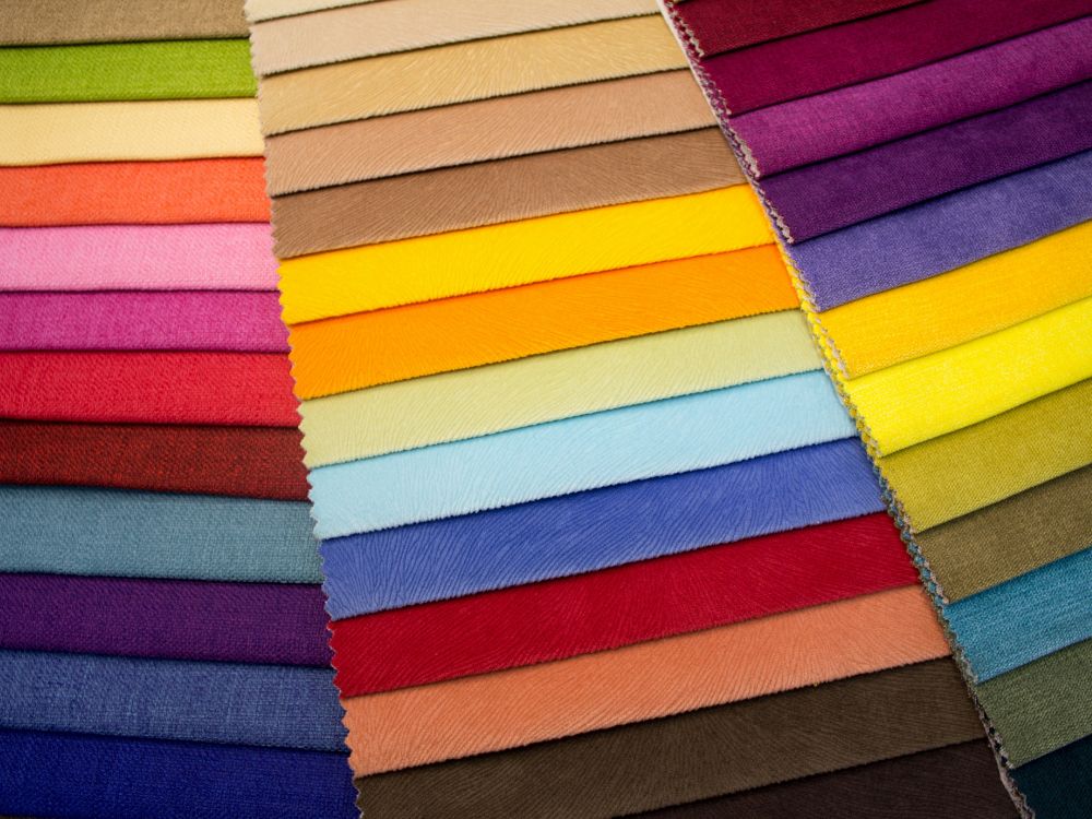 Colorful array of fabric swatches in various shades including reds, pinks, blues, and yellows arranged in a gradient pattern.