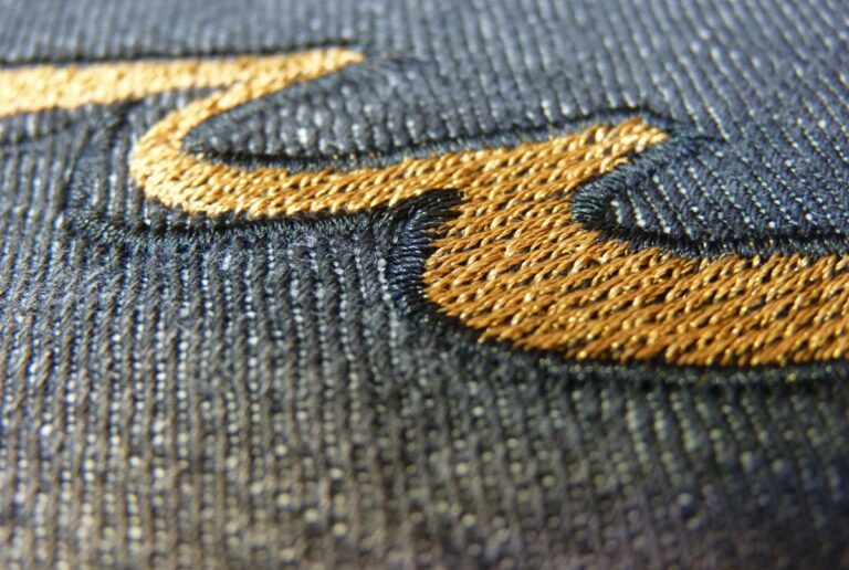 Close-up of gold embroidery stitched into dark denim fabric