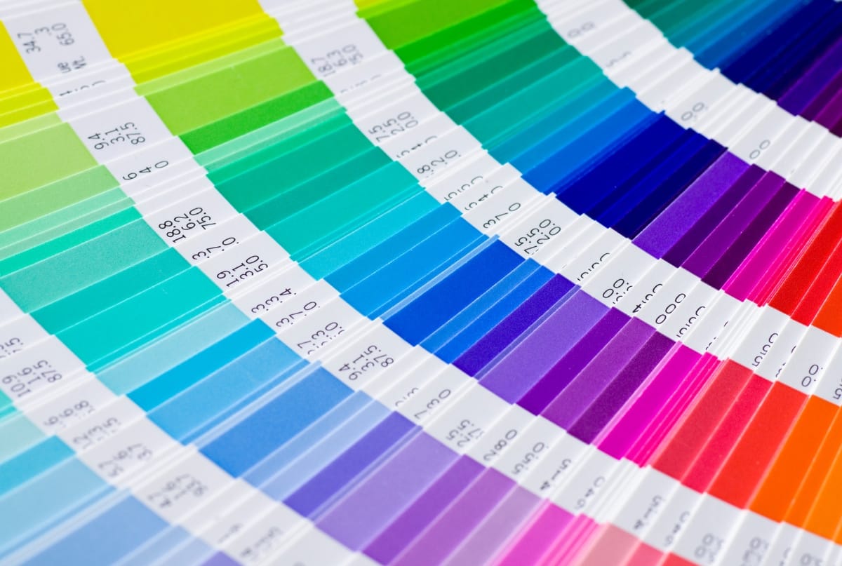 A close-up of a color fan deck displaying a gradient of vibrant paint swatches, arranged in circular arcs with labels.