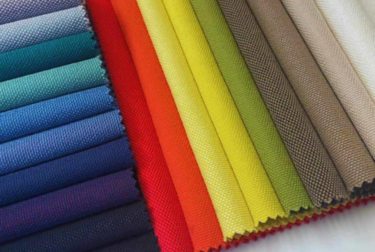A neatly folded fan of colorful fabric swatches arranged from shades of blue to yellow and neutral tones, showing different textures and patterns.