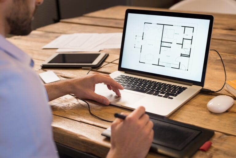 Designer working on a laptop with a drawing tablet at a wooden desk