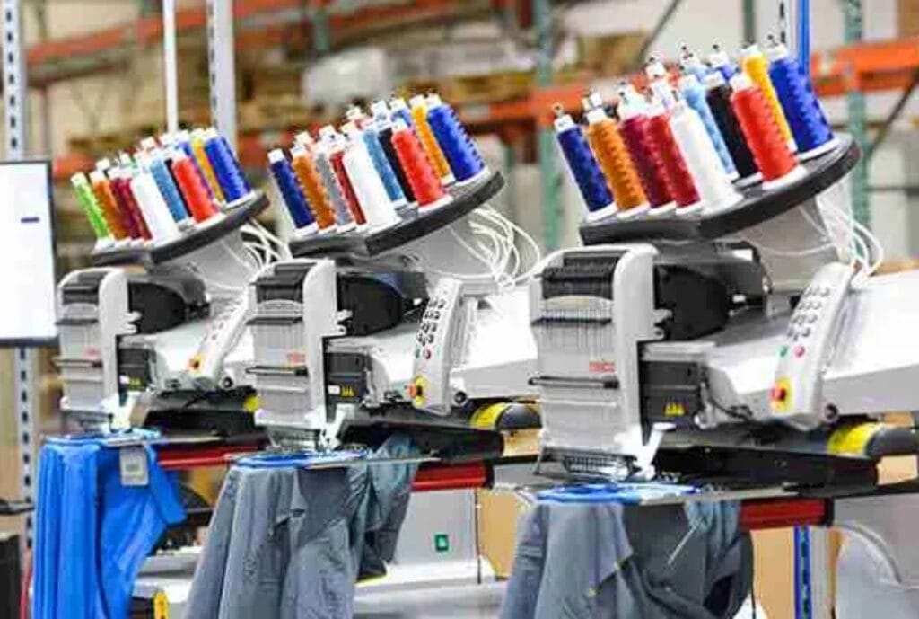 Three multi-head embroidery machines in a factory setting, with colorful threads loaded, used for large-scale garment embroidery.