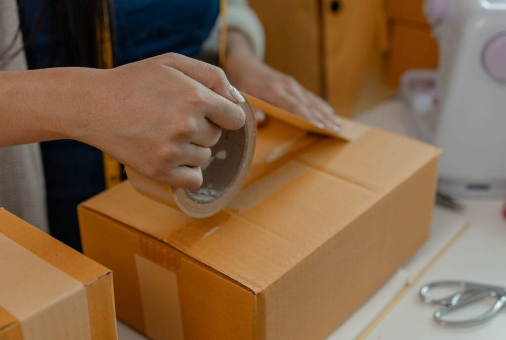 A person taping a cardboard box, illustrating packaging process in logistics.