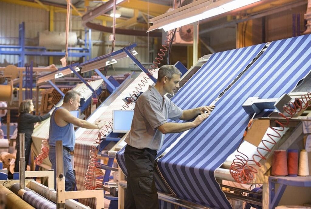 Two operators checking striped fabric on inspection machines in a textile mill