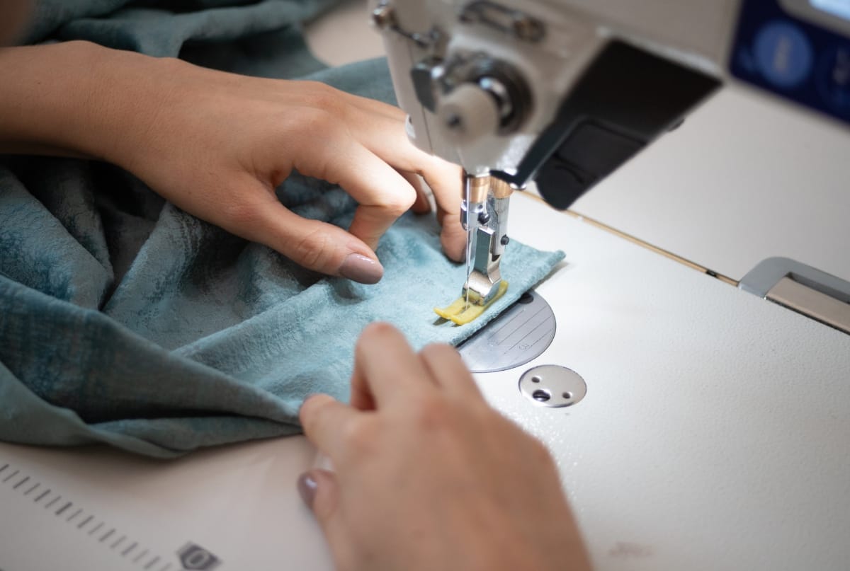 A person sewing fabric using a sewing machine, focusing on the needle and fabric under the presser foot.