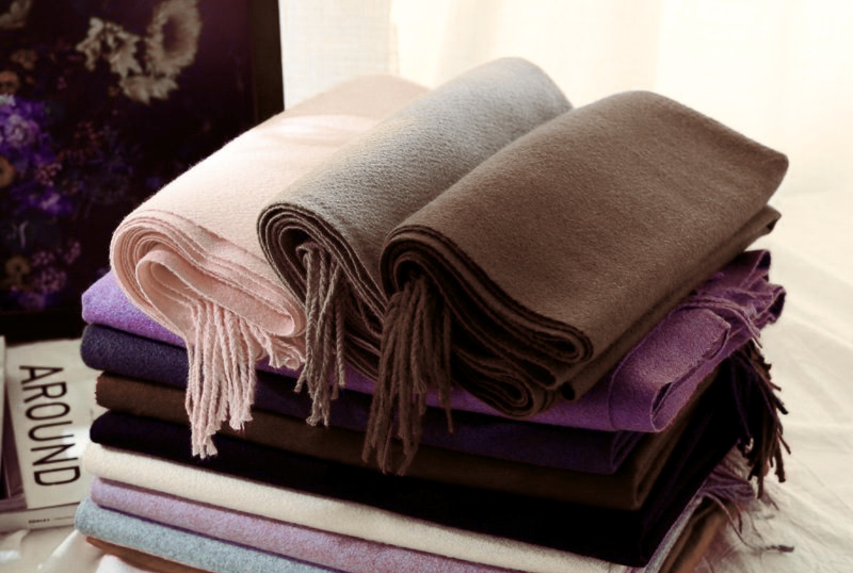 A close-up image of wool scarves in various colors and textures, showcasing the craftsmanship involved in their manufacturing process.