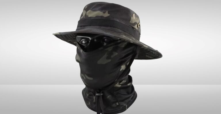 Eine Kombination aus einer getarnten Sturmhaube und einer Mütze. Die Sturmhaube bedeckt das Gesicht, sodass nur die Augen sichtbar sind, und die Mütze im Bucket-Stil mit Camouflage-Muster sitzt auf dem Kopf.