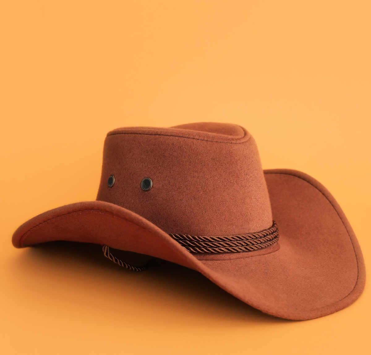 A brown felt cowboy hat with a braided black-and-brown hatband, set against a warm orange background.