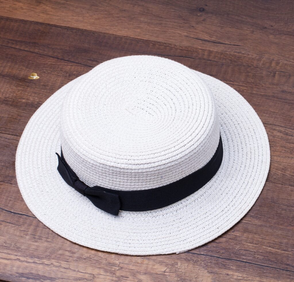A white straw hat with a black band resting on a wooden surface.