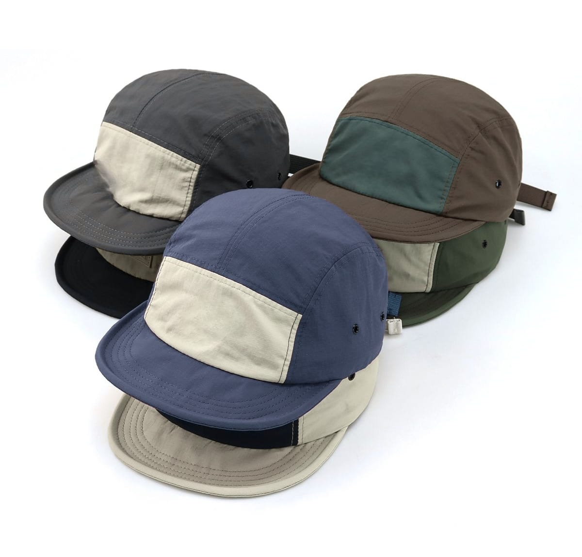 “A row of five-panel caps in varied two-tone colors arranged in a diagonal line, showing cream, gray, blue, brown, and green panels.”