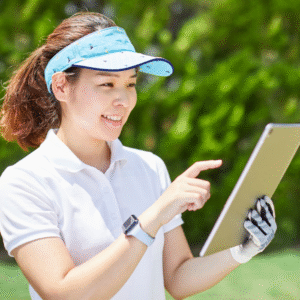 A smiling woman wearing a light blue visor and white polo shirt, outdoors on a sunny day, holding and interacting with a tablet.