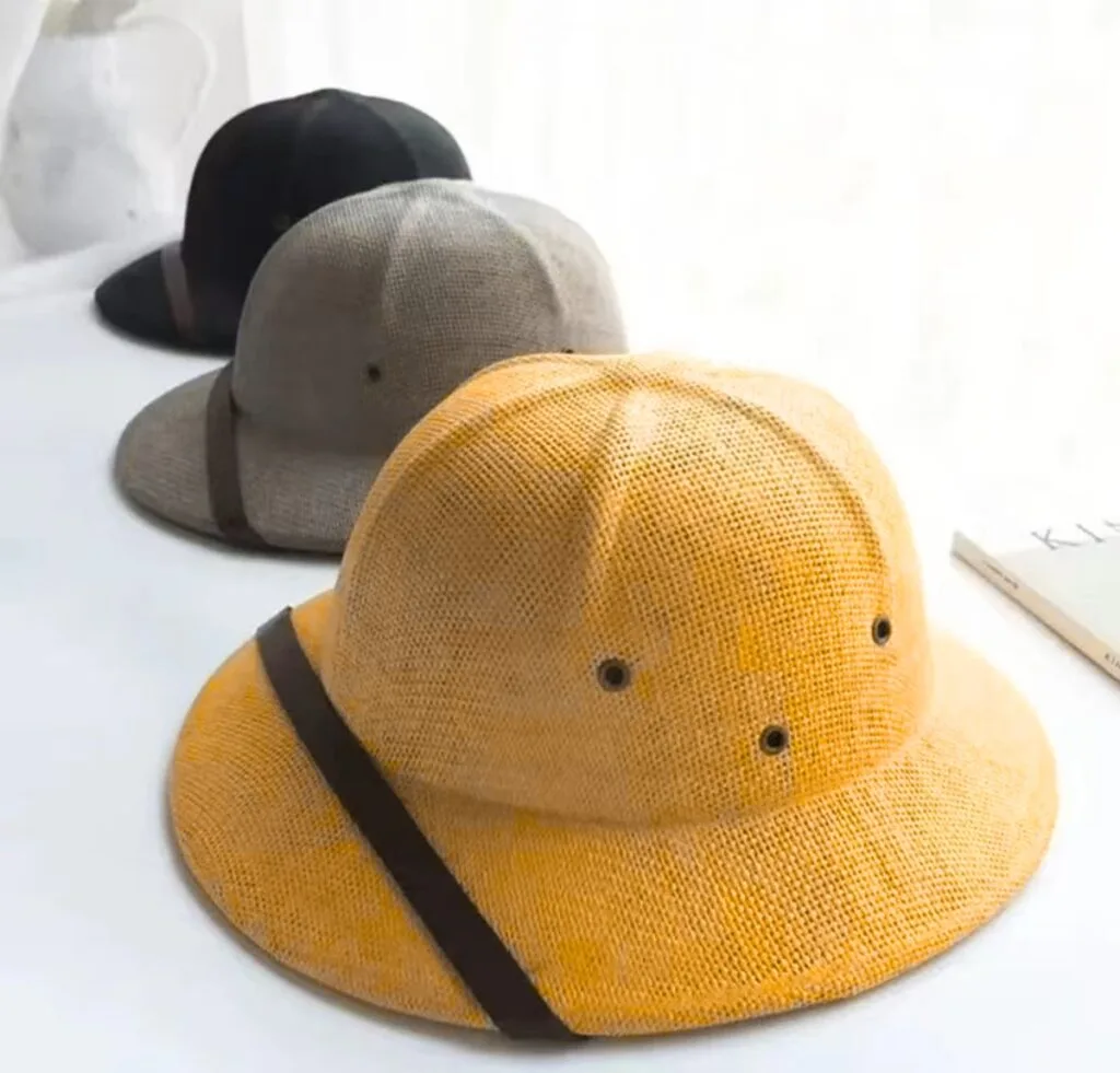 A trio of stylish hats in different colors (mustard yellow in the foreground, gray in the middle, black in the back) arranged in a row on a white surface, with a strap detail on each.