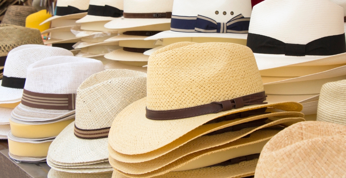 Eine Ausstellung von Stroh-Cloche-Hüten, die in einem Hutgeschäft gestapelt und arrangiert sind, mit natürlichen Beigetönen, gewebten Texturen und einigen Hüten mit schlichten Bändern.